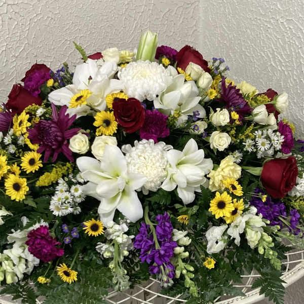 Large mixed floral arrangement with white lilies, red roses, and purple flowers