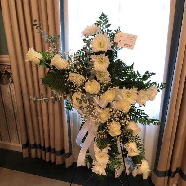 White floral standing spray on an easel with ribbon accents