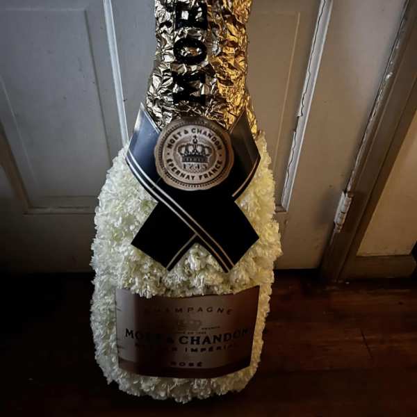 White floral champagne bottle arrangement with black ribbon and gold foil wrap