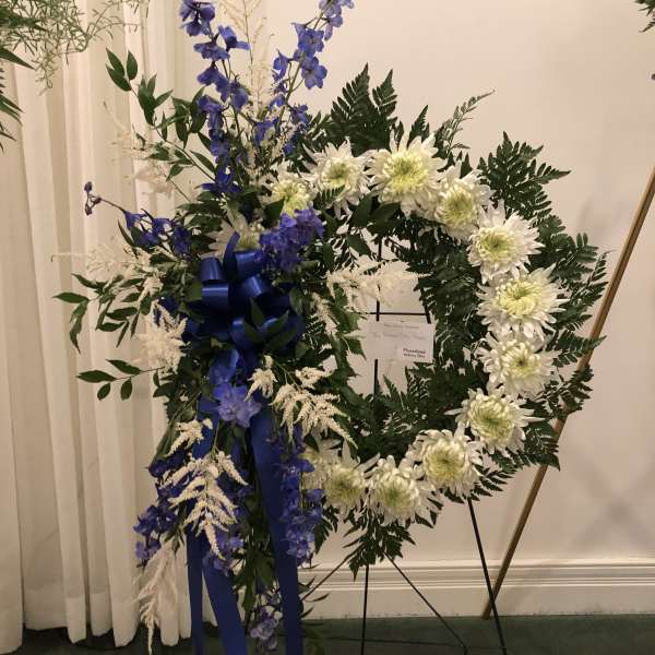 White chrysanthemum wreath with blue flowers and ribbon on a stand