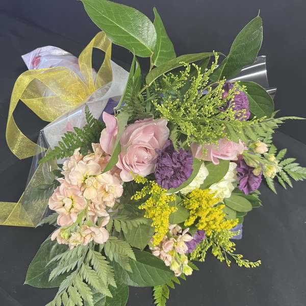 Bouquet of pink and purple flowers wrapped in clear plastic with a yellow ribbon