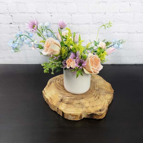 Pastel flower arrangement in a white vase on a wood slice