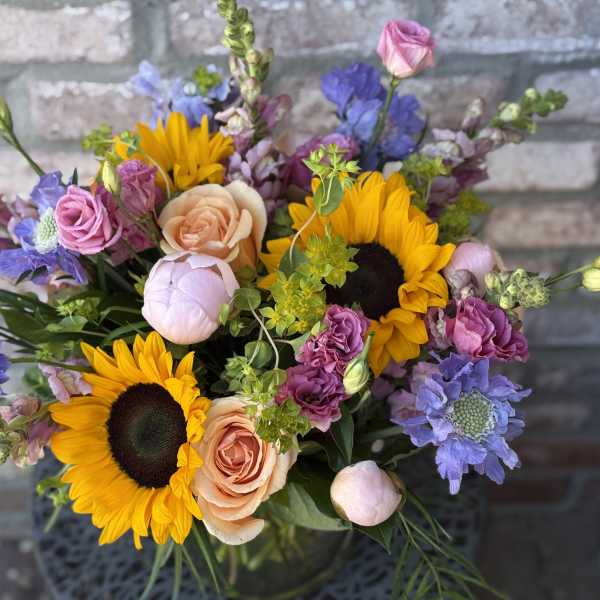 Mixed bouquet with sunflowers, peach roses, and purple blooms in a vase