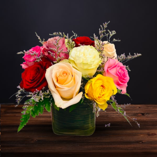 Mixed roses in a green square vase on a wooden surface