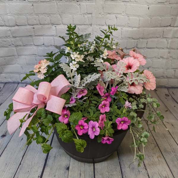 Mixed pink and white flowers in a black planter with a pink bow