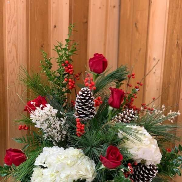 Holiday arrangement with red roses, white hydrangeas, pinecones, and berries