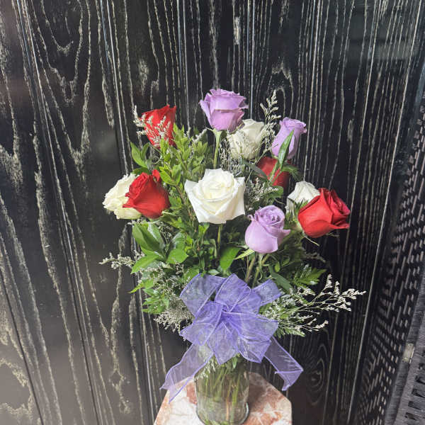 Bouquet of red, white, and lavender roses in a glass vase with a purple bow.