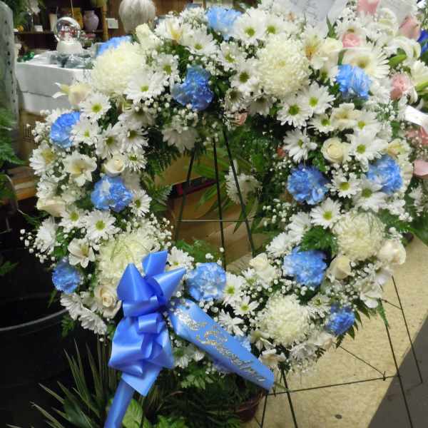 Heart-shaped floral wreath with white and blue flowers on a stand
