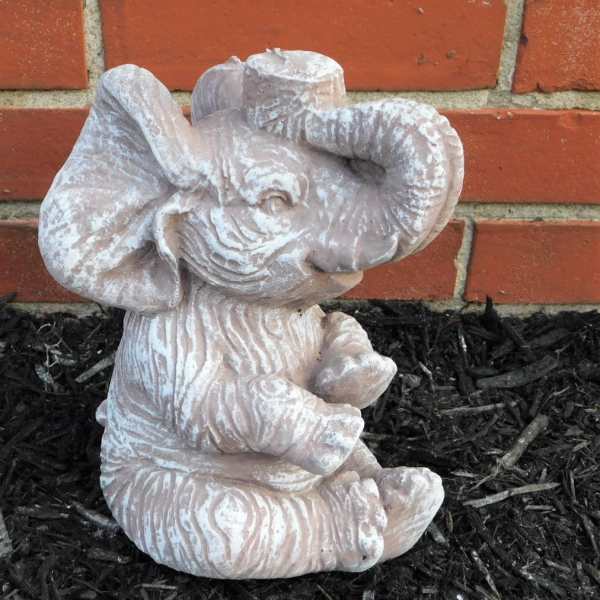 Small elephant figurine in a garden bed against a brick wall