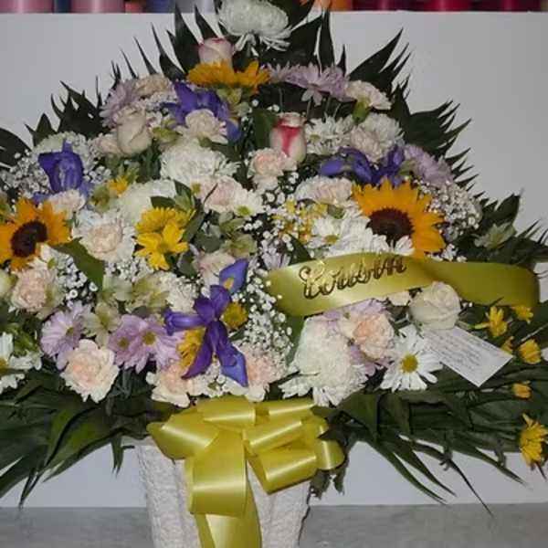 Large mixed flower arrangement in a white basket with yellow ribbon