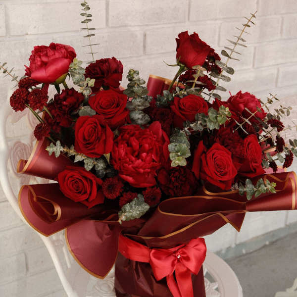 Red rose bouquet with dark red blooms and eucalyptus in burgundy wrap