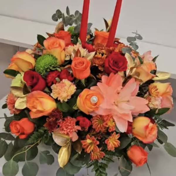 Round floral arrangement with orange and red roses and two red taper candles