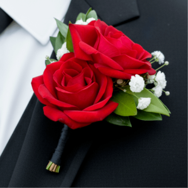 Red rose boutonniere with small white accent flowers pinned to a black suit lapel