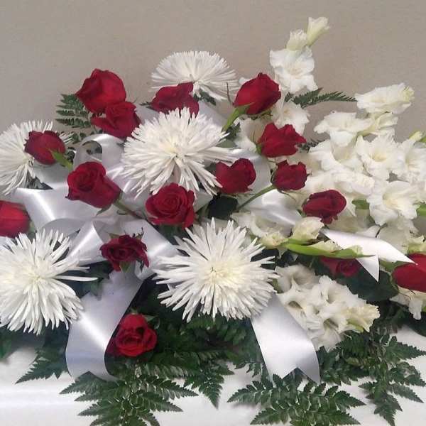 Red roses and white flowers arranged with white ribbon on a table