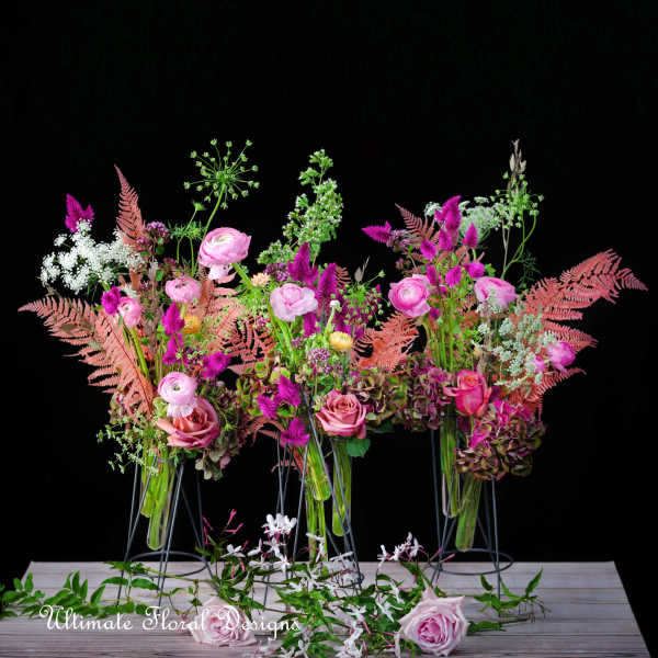 Pink and purple floral arrangements in glass vases on metal stands