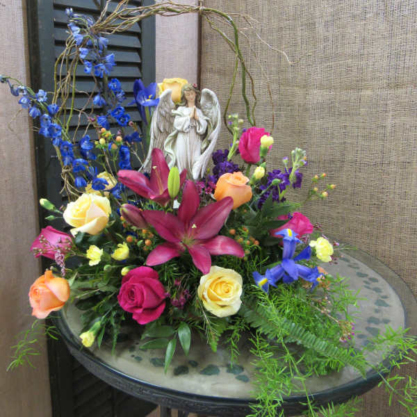 Mixed bouquet with roses, lilies, and an angel figurine in a low vase