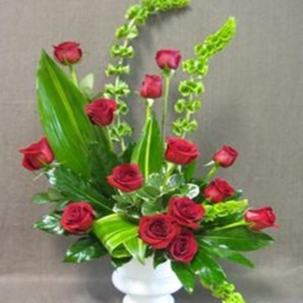 Red roses arranged in a white vase with tall green foliage