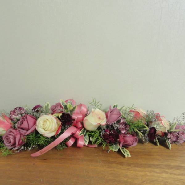Low floral arrangement with pink and cream roses and a pink ribbon