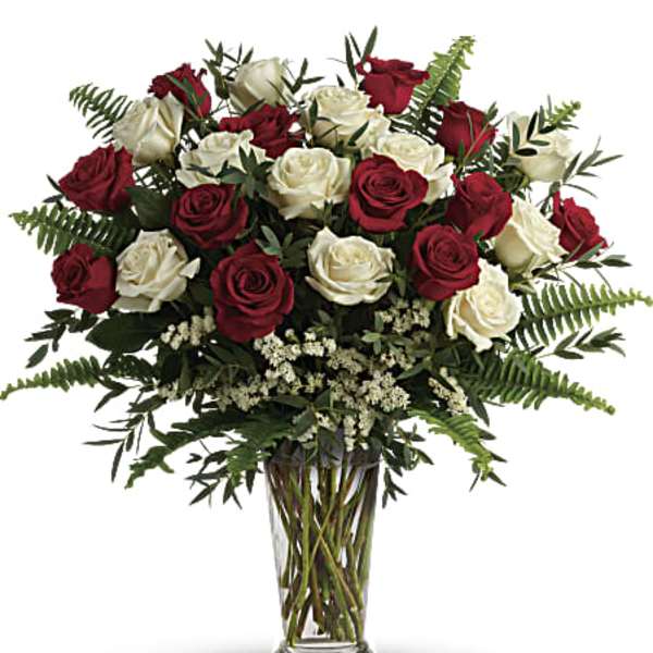 Tall arrangement of red and white roses with ferns in a clear glass vase