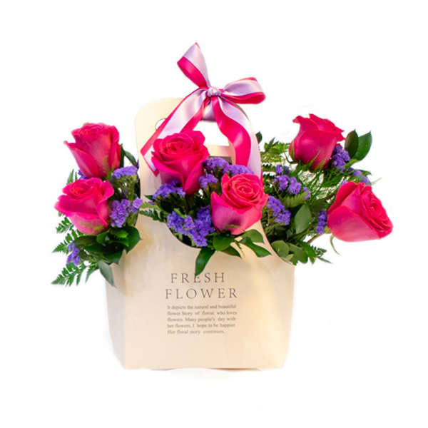 Pink roses in a cream gift bag with a ribbon bow