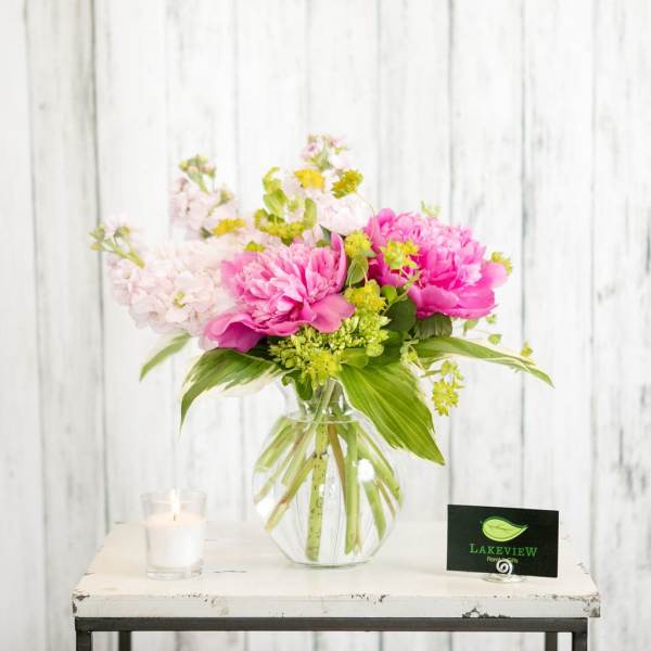 Pink peonies and pale blossoms in a clear glass vase with a candle nearby
