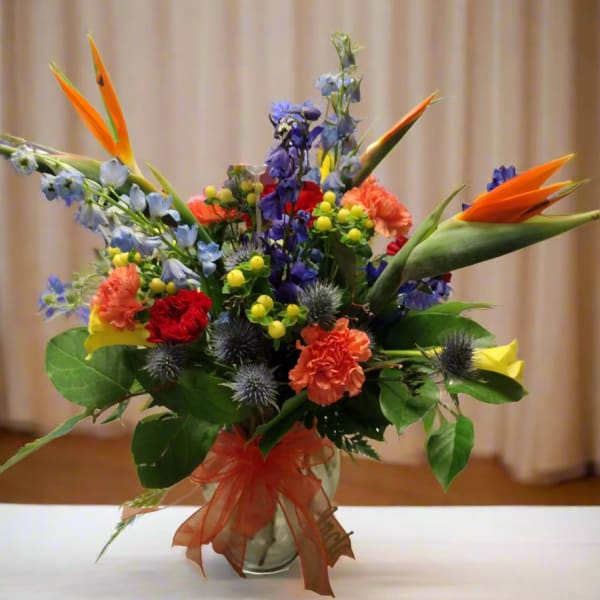 Colorful tropical bouquet in a glass vase with orange bird-of-paradise blooms