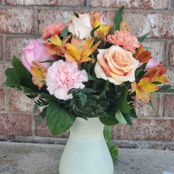 Bouquet of peach and pink roses with carnations in a white vase
