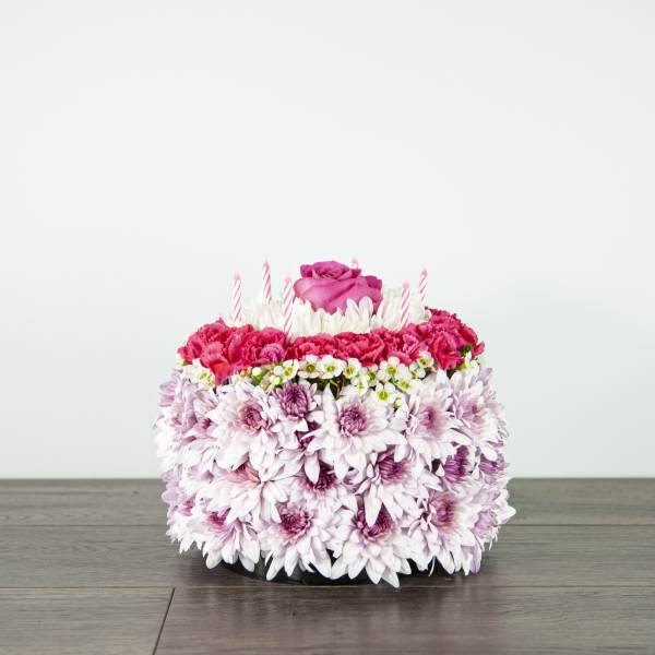 Round floral cake with pink roses, carnations, and candles