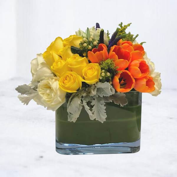 Yellow roses and orange tulips in a square glass vase