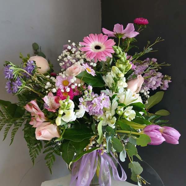 Mixed pink and lavender flower arrangement in a glass vase with a purple ribbon