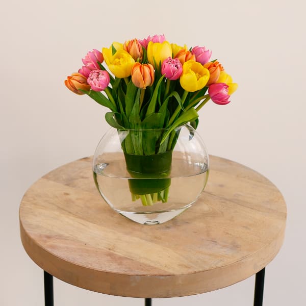 Bouquet of pink, yellow, and orange tulips in a round glass vase
