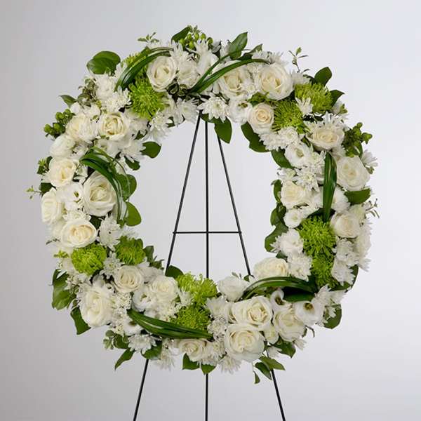 White floral wreath on a black stand with green accents