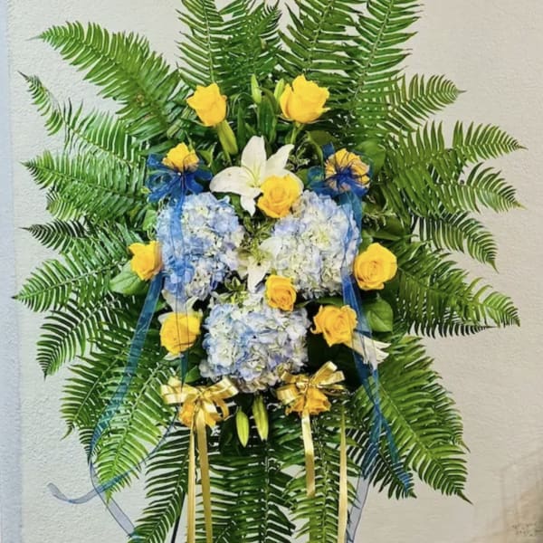 Standing floral spray with yellow roses, white lilies, and blue hydrangeas
