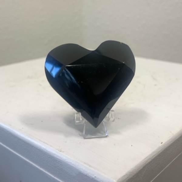 Black faceted heart-shaped decorative object on a clear stand