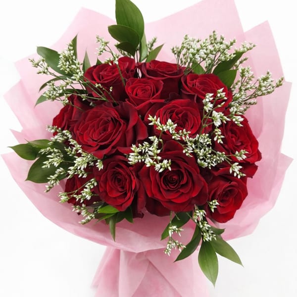 Bouquet of red roses with white filler flowers wrapped in pink paper