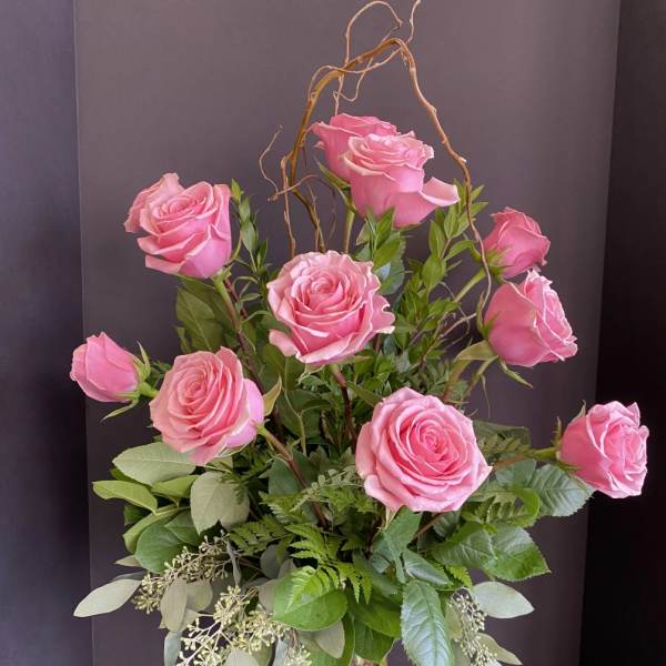 Pink roses arranged in a clear glass vase with mixed greenery