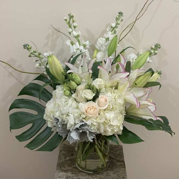 White and blush floral arrangement in a glass vase with large tropical leaves