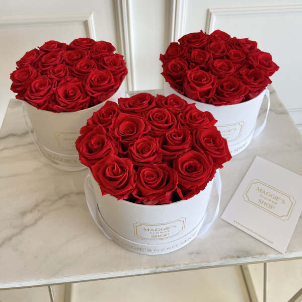 Three round boxes filled with red roses on a marble surface