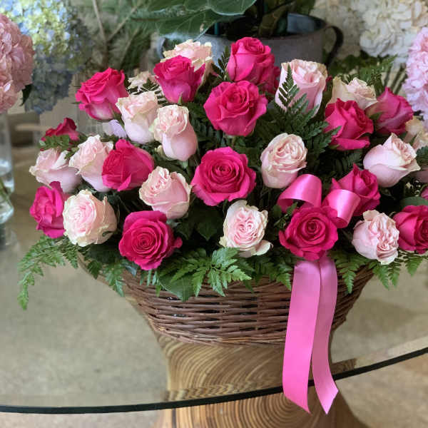 Basket arrangement of pink and white roses with a pink ribbon