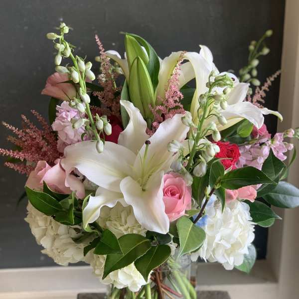 Bouquet of white lilies, pink roses, and white hydrangeas in a glass vase.