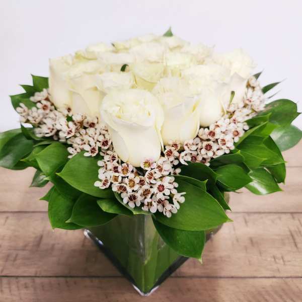 White rose bouquet in a clear glass vase with green leaves