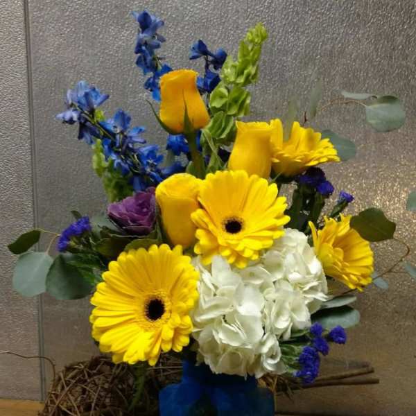 Bouquet of yellow gerbera daisies, roses, and white hydrangea in a glass vase
