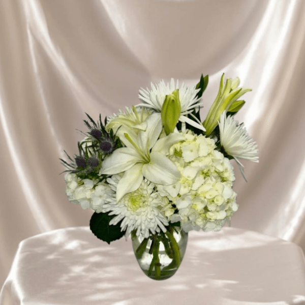 White floral arrangement in a clear glass vase with lilies and mums