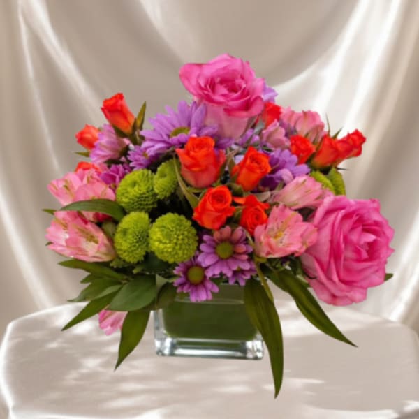 Pink and orange mixed flower arrangement in a square glass vase