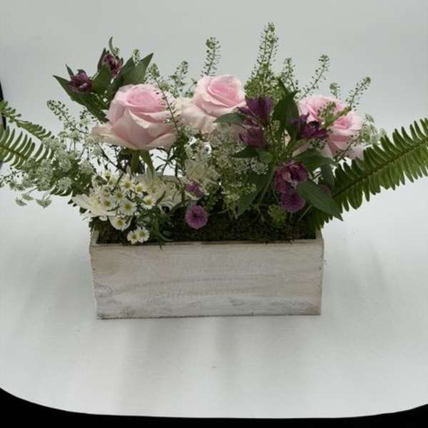 Pink roses and purple flowers arranged in a rectangular wooden box