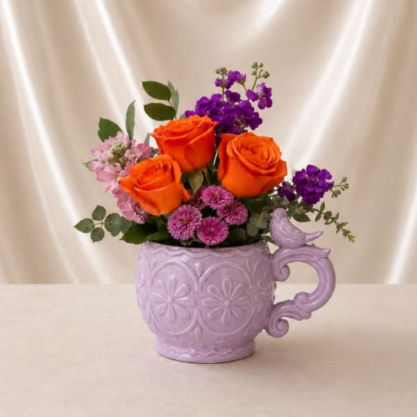 Orange roses and purple flowers in a lavender mug vase