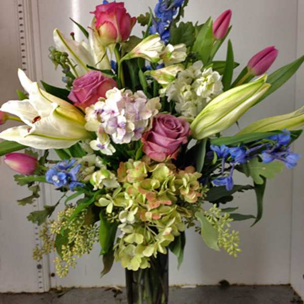 Bouquet of pink roses, white lilies, and blue flowers in a glass vase