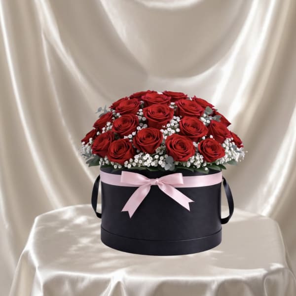 Red roses arranged in a black round box with a pink ribbon