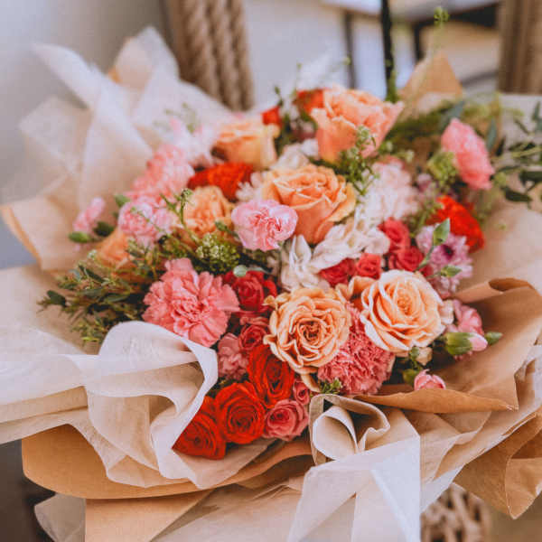 Bouquet of peach, pink, and red roses with carnations wrapped in brown paper