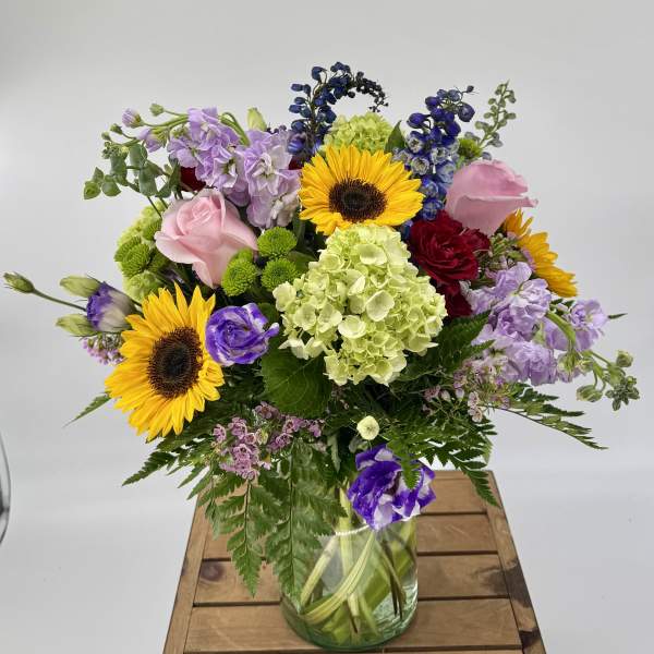 Mixed bouquet with sunflowers, roses, hydrangea and purple blooms in a clear glass vase